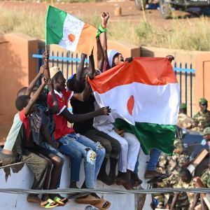 Joukko nuoria pitää Nigerin lippua. Taustalla sotilaita.