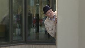 En man kollar om kusten är klar, om han kan rymma, från en performance 2018 om Åbo fångläger. En man i svart hatt tittar om kusten är klar, om han kan rymma (från en performance om Åbo fångläger).