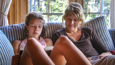 Sara sitter i soffan med sin lillasyster som läser en bok.