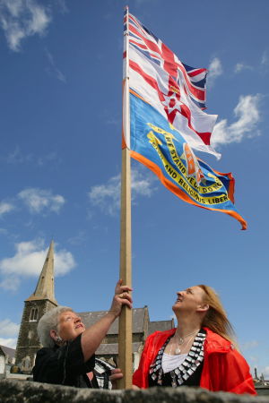 Två kvinnor med den brittiska flaggan, den nordirländska flaggan och Oranieordens egen flagga inför ordens parad. Två kvinnor hissar den brittiska och Oranieordens flagga inför paradsäongen i Nordirland