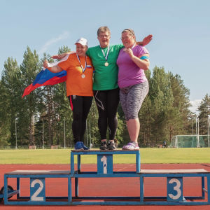 Kolme naista tuulettaa urheilukentällä palkintokorokkeella seisten, mitalit kaulassaan, yhdellä olkapäillä Venäjän lippu.
