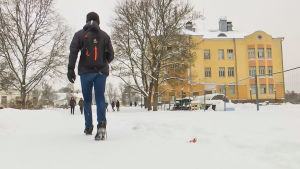 Glada vi till skolan gå...Lovisa gymnasium i sikte. Axel går till gymnasiet. Det är snö på marken. Han har sin ryggsäck på ryggen.