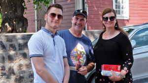 Marc-Benedict Schäfer, Olaf Schäfer och Britta Schäfer blev intresserade av Finland på en mässa. Två män och en kvinna står framför ett rött trähus i Gamla stan i Borgå. De har sommarkläder på sig och ser glada ut.