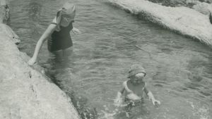 Vattendrag har varit avgörande för både uppkomst av jordbruk och skötsel av hygien. Här badar en kvinna och ett barn i lågvatten vid strandklippor i Swakopmund, Namibia. Året är 1953. Svartvit bild på kvinna och barn som badar vid strandklippor i Swakopmund i Namibia.