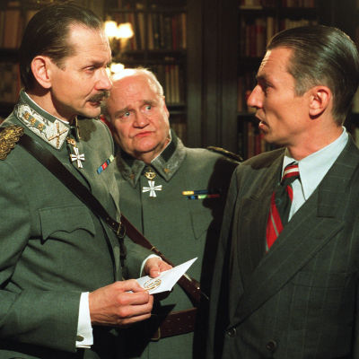 Vasemmalla Asko Sarkola, joka esittää Mannerheimiä. Takana keskellä Oiva Lohtander, joka esittää Walldenia. Äärimmäisenä oikealla on Robert Enckell, joka esittää eversti-luutnantti Josef Veltjenssiä.