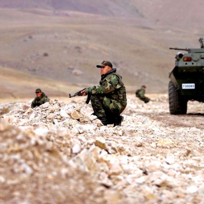 Soldater i kamouflagedräkt står på knä runt ett pansarfordon.