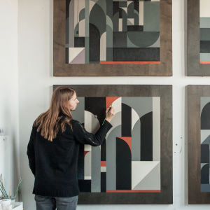 Taiteilija Tony Sjöman maalaa ateljeessa abstraktia taideteostaan, joka on ripustettu seinälle kolmen muun samantyyppisen taulun kanssa.