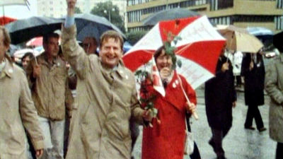 Olof och Lisbet Palme under ett rödvitt paraply med blommor i händerna.