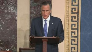 Mitt Romney förklarade sitt beslut i sitt tal inför senaten. Mitt Romney, en äldre man med grått hår och blå kostym står vid ett talarpodie.