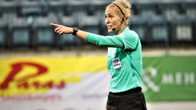 Lina i färd med att utfärda en dom på fotbollsplanen. Hon pekar mot något håll och ser bestämd ut, med headset på huvudet.
