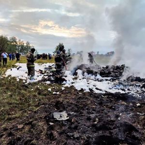 Kuva maastosta, jonne lentokoneen kerrotaan pudonneen. Maassa on valkoista sammutusvaahtoa. Koneen jäänteistä nousee savua. Tapahtumapaikalla on palomiehiä ja muita ihmisiä. 