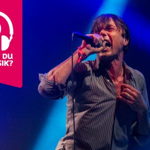 Brett Anderson sjunger i en mikrofon som han håller i handen.