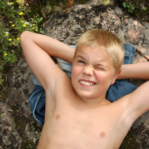 Näyttelijä Topi Raulo makailee selällään farkkutakin päällä kalliolla Paavo Pahtajärven roolissa kesäisenä päivänä.