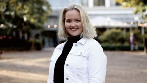 Soini lyfter upp att valet är väldigt dyrt, särskilt för en kandidat i Helsingfors, och att många dyra annonsplatser är svåra eller omöjliga att avboka. En blond kvinna iklädd en vit jeansjacka och en svart polotröja står utomhus och ler in i kameran. Bakgrunden är ofokuserad, men ser ut som ett hus.