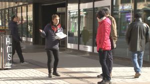 Konsta trivs med sitt jobb, berättar han. En gatuförsäljare pratar med en dam och en herre på en gågata.