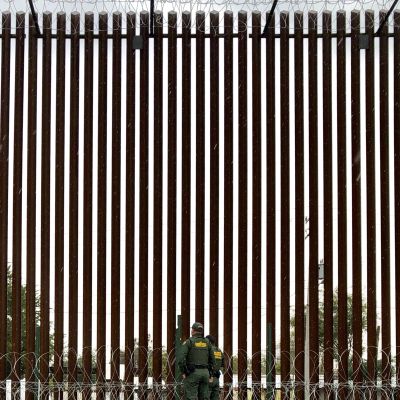 Två poliser ur gränsbevakningen vdi gränsmuren mot Mexiko. Den är fyra gånger högre än de.
