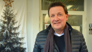 Christer Weckström flyttar sitt företag till Sibbo. En man i ytterkläder står inomhus. Han tittar in i kameran och ler lite. Bakom honom skymtar en julgran.