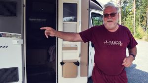 För Jari Siltala är Spaniens campingplatser mer bekanta än skärgården. Jari Siltala i vinröda kläder med portugals flagga, står framför sin husvagn och pekar åt vänster och skrattar.