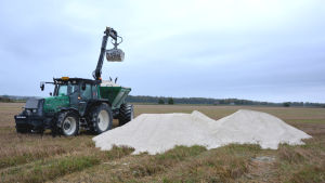 Strukturkalken lyfts upp för att spridas ut. En traktor med grävskopa håller på att lyfta upp strukturkalk på släpkärran.