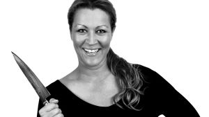Lotten Lindborg-Suhonen lagar mat tillsammans med Sonja Kailassaari. Kocken Lotten Lindborg-Suhonen ler och poserar med en kniv i handen.