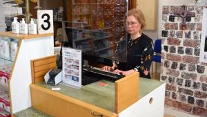 Vuokko Mustonen har ordnat med plexiglas i apotekets kassa. Vuokko Mustonen bakom en plexiskyddsskiva i Dalsbruks apotek.