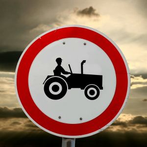 Skylt av en bonde som kör traktor. Mörka moln i bakgrunden.
