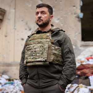 Volodymyr Zelenskyi seisoo vakavailmeisenä sodan tuhoaman rakennuksen edessä.