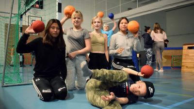 Åtta ungdomar  uppställda i en gympasal med bollar i händerna.