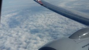 Första gången uppe bland molnen. Bild tagen ut från flygplansfönster med vinge, motor och moln.