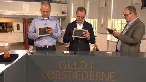 Uppköparna skriver sina bud på tavlor i hopp om en god affär. Tre värderare står vid ett bord och skriver sina bud på små tavlor.