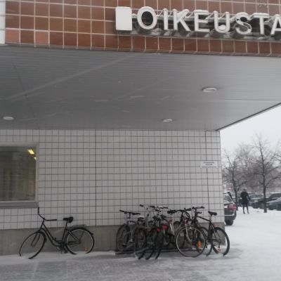 Oulun oikeustalon ulkoseinä talvella ja taustalla lehdettömiä puita.