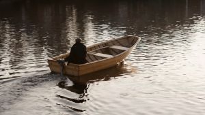 Dok: Herbert ja Alice. Man sitter i en båt med aktersnurra och åker bortåt från fotografen