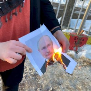 Henkilö pitää kädessään palavaa Vladimir Putinin valokuvaa.