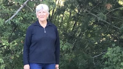 En kvinna står utomhus med en hund i koppel.