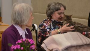 Festens mjukaste gäst. Cia Frejborg tog med sig sin katt till festen. Både Berit Eklund och Gun-Maj Rehnberg fick umgås med katten och ha den i famnen. Gun-Maj Rehnberg har en katt i famnen, tittar ner på katten och pajar den. Berit Eklund sitter bredvid och tittar på.