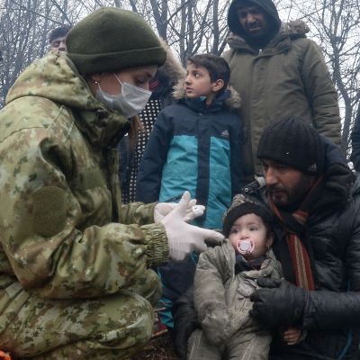 En läkare utför hälsokoll på en pappa och hans barn i ett migrantläger. 