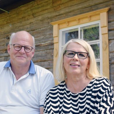 Tuula ja Reijo Karhinen Suomi 100 vuotta-hirsitalon edustalla.