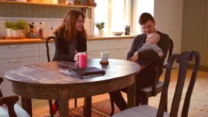 Familjen har klarat sig bra igenom renoveringen så här långt. Henrika och Mathias Gustafsson sitter i ett mysigt, grönt kök med sin son i famnen vid köksbordet.