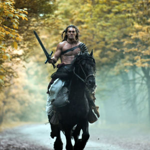 En barbröstad man på hästrygg håller ett långt svärd i handen. 