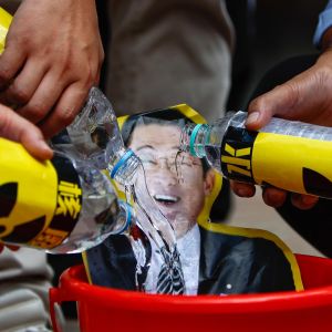 Tre vattenflaskor med symboler för radioaktivitet töms över ett porträtt av Japans premiärminister.