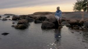 Irmelin Sandman Lilius sitter och väntar på Havshäxan. Irmelin Sandman Lilius sitter på en sten i havet.