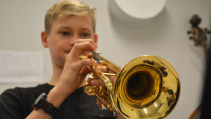 Det borde satsas mer för att öka barn och ungas möjligheter att delta i kultur- och konstutbildningar menar Nygård-Fagerudd. Närbild på en trumpet. I bakgrunden synns en pojke som spelar.