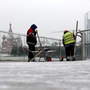 Kaksi katutyöntekijää on hommissa lumisessa Moskovassa. Taustalla näkyy Kremlin muuria, torneja ja Pyhän Vasilin katedraali.