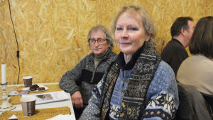 Susan Hamro-Drotz Kassinen och Hannu Kassinen har också kommit till invånarmötet. Hamro-Drotz Kassinen tycker det är synd att det inte längre finns någon allmän badstrand i Gumbostrand. Hon nämner också butiksbåten som viktig för invånarna. En äldre kvinna och en äldre man sitter vid ett bord. Framför sig har de papper och kaffekoppar.