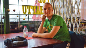 Ville Tuominen kanske själv behöver använda krematoriets tjänster i något skede. En ung man sitter vid ett bord på en bar. Han vilar kinden mot handen och tittar in i kameran. Framför honom ligger en mössa och står en vattenflaska.