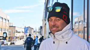 Staffan Söderström. En medelålders man i mössa och vit jacka tittar in i kameran. Bakom honom syns Borgå centrum.