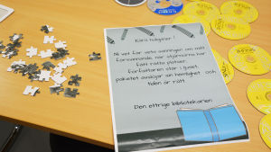 Efter en stund hittar spelarna den viktigaste ledtråden som berättar hur de ska gå vidare. Klicka på bilden för att se den som stor. På ett träbord ligger cd-skivor och pusselbitar utspridda. Mitt på bordet ligger ett papper där det står tips på hur spelarna kommer vidare.
