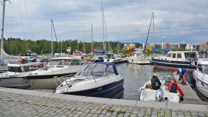 På bilden syns flera rader med segelbåtar och motorbåtar i Borgå å. Längst nere till höger i bilden finns en öppen motorbåt med några personer i. En man håller på att förtöja båten.