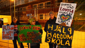 Många demonstrerade emot skolindragningarna under budgetmötet. En kvinna och flera barn står utomhus och håller i skyltar. På skyltarna står det slagord som hjälp haddom skola.