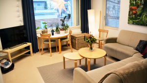 Det går också att träffa socialarbetare i social- och krisjourens egna lokaler. Bild av ett vardagsrum i ljusa färger. En beige hörnsoffa och några runda bord finns framför en television. I fönstret hänger en julstjärna.
